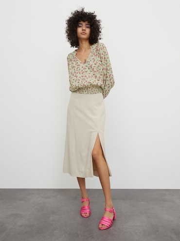 Mujer con falda midi color crema con abertura lateral de la marca EDITED