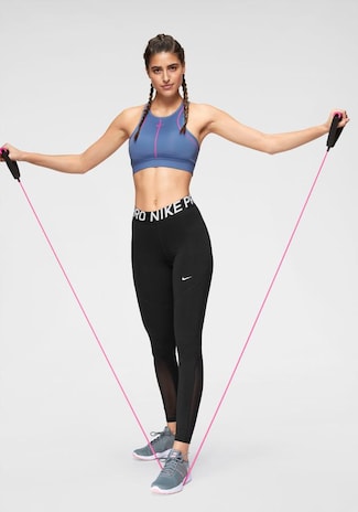 Mujer haciendo deporte con bandas elásticas, top azul marino y pantalones de deporte negros largos marca Nike