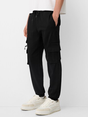 Bershka Tapered Cargo trousers in Black: front