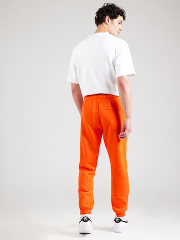 Nike Sportswear Tapered Housut 'Club Fleece' värissä oranssi