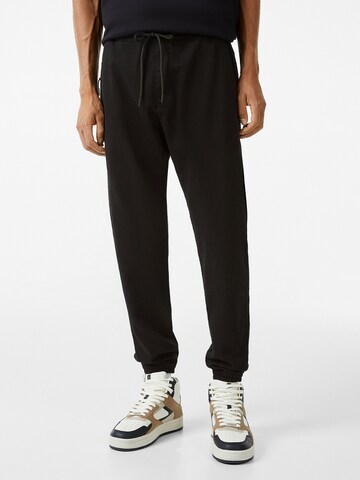 Bershka Tapered Trousers in Black: front