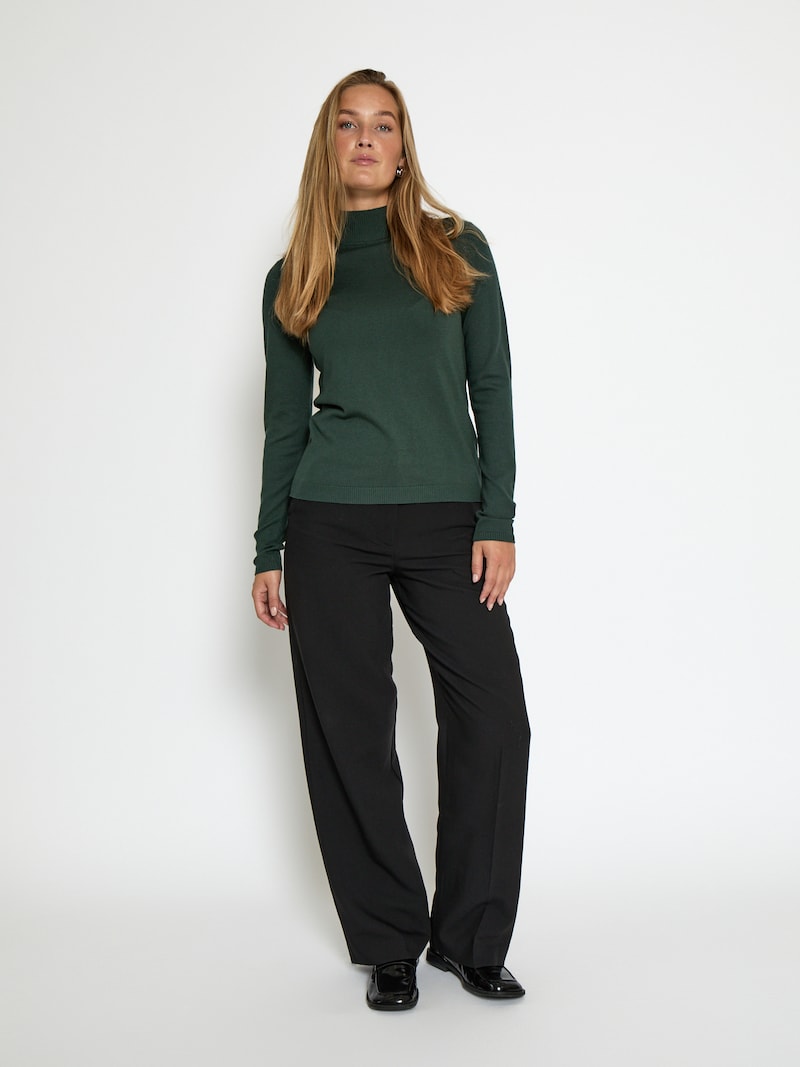 Woman in forest green turtleneck sweater with black satin trousers