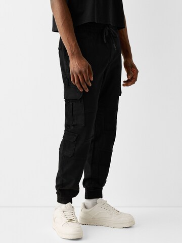 Bershka Tapered Cargo Pants in Black: front